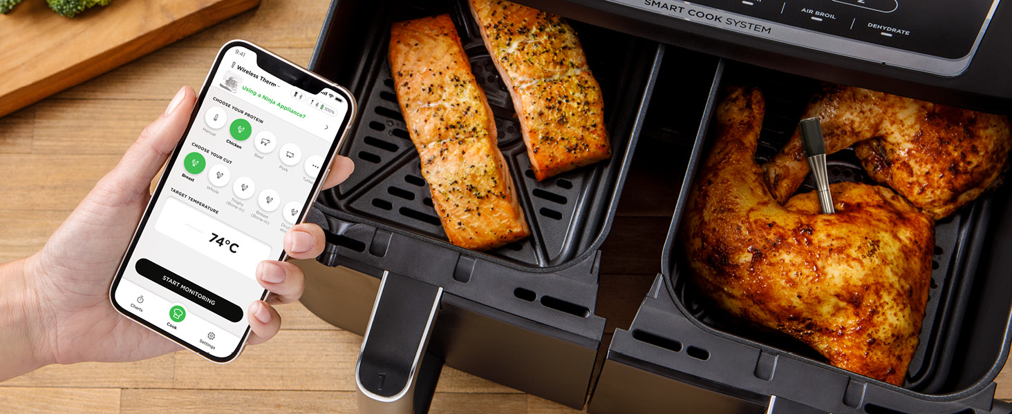 Das Smartphone zeigt eine App-Oberfläche neben der Heißluftfritteuse an, die gekochte Lebensmittel enthält, einschließlich etwas, das anscheinend Hühnchen ist.